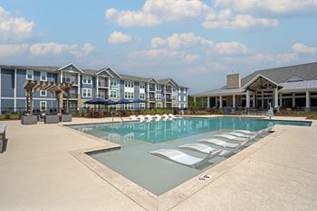 A large swimming pool in front of a building with a blue sky and clouds in the background.